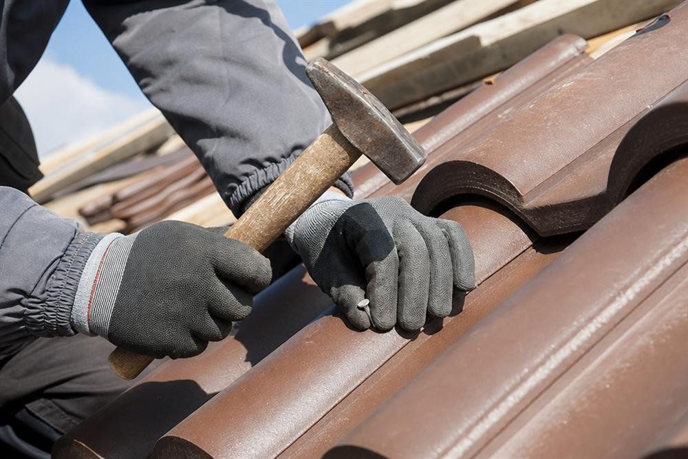 Roofer's hands securing a roof tile with a hammer